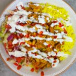 marinated chicken is cooked and then served with rice, salad and white sauce