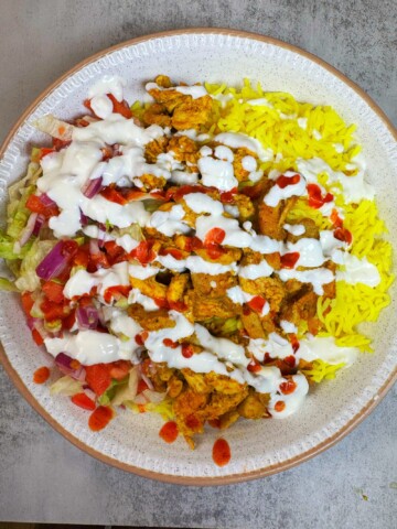 marinated chicken is cooked and then served with rice, salad and white sauce