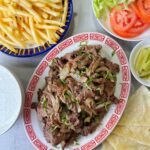 A plate full of authentic beef shawarma slices, along with fries and salad